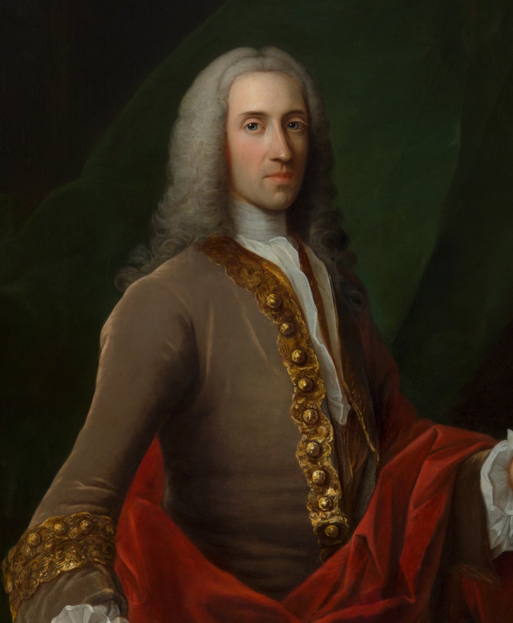 An 18th-century oil portrait depicting a wigged gentleman in a brown coat seated beside open books, enclosed in a carved giltwood frame. View VI