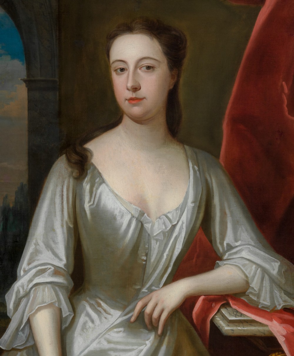 A portrait depicting a woman in a silver satin dress seated next to draped red fabric, enclosed within an ornate carved gold frame. View VI
