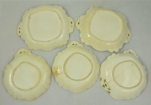 fig 1. A five-piece English Rococo porcelain dessert service featuring cream-coloured shaped dishes hand-painted with green foliage, floral motifs, and gilt scalloped rims.