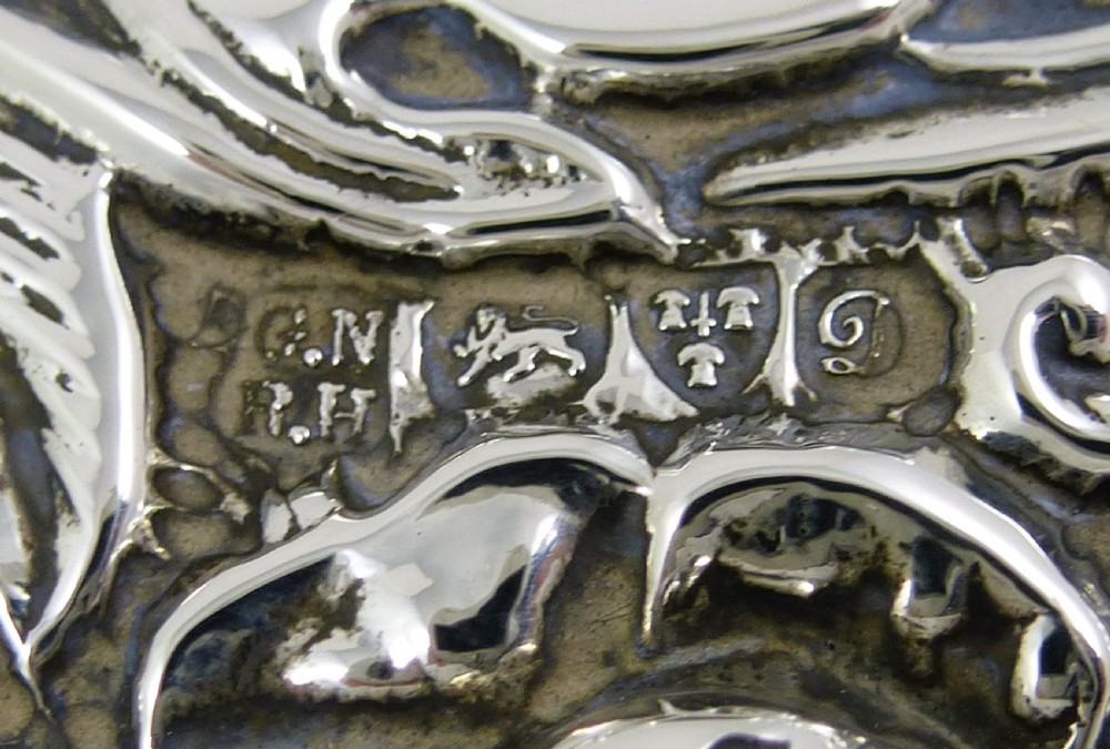 An Edwardian sterling silver hand mirror decorated with repousse floral scrollwork and a central engraved cartouche. View III