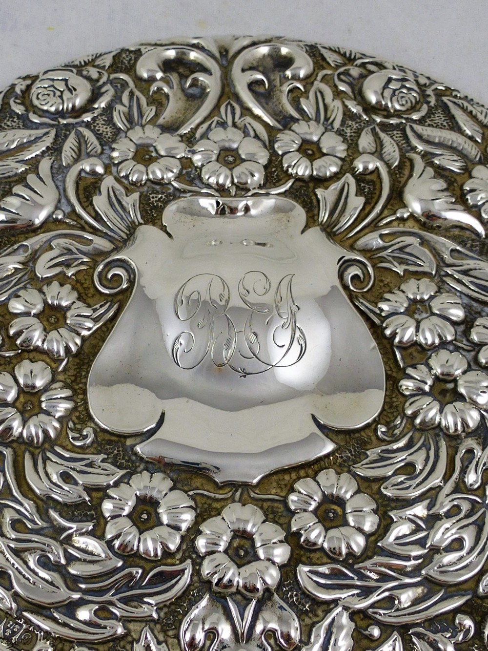 An Edwardian sterling silver hand mirror decorated with repousse floral scrollwork and a central engraved cartouche. View VII