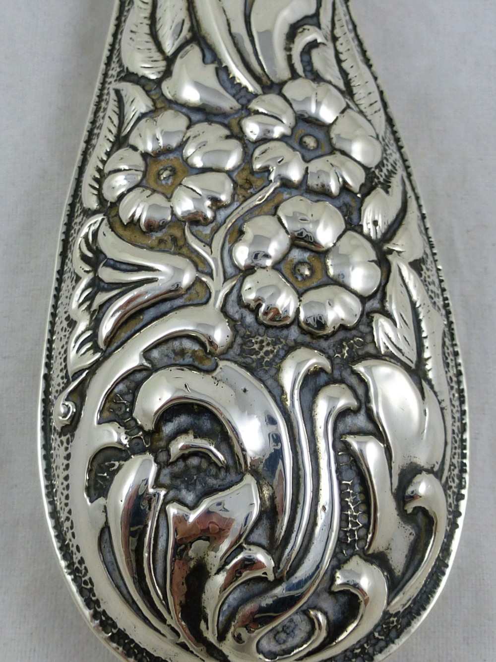 An Edwardian sterling silver hand mirror decorated with repousse floral scrollwork and a central engraved cartouche. View VIII
