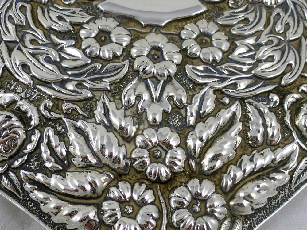 An Edwardian sterling silver hand mirror decorated with repousse floral scrollwork and a central engraved cartouche. View IX