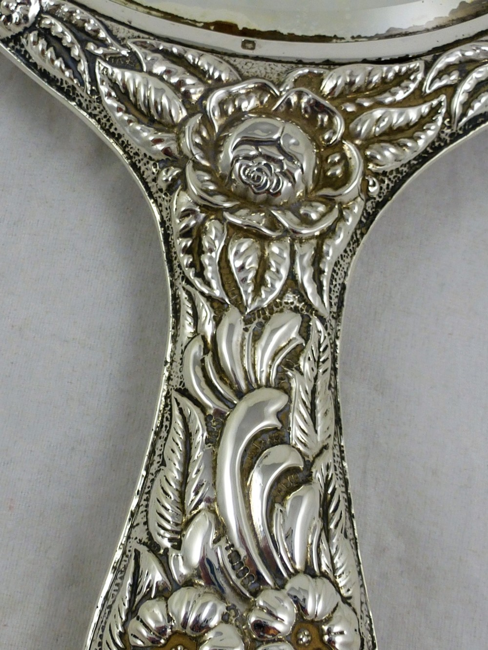 An Edwardian sterling silver hand mirror decorated with repousse floral scrollwork and a central engraved cartouche. View XI
