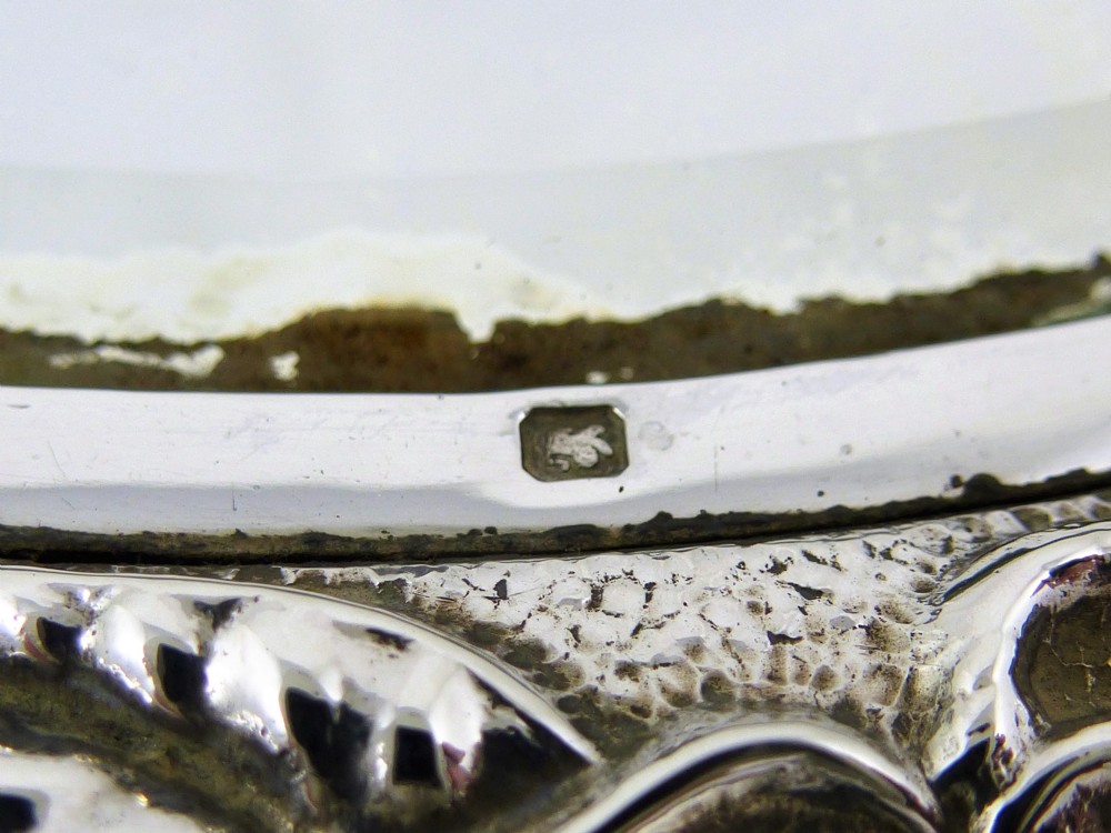 An Edwardian sterling silver hand mirror decorated with repousse floral scrollwork and a central engraved cartouche. View XII