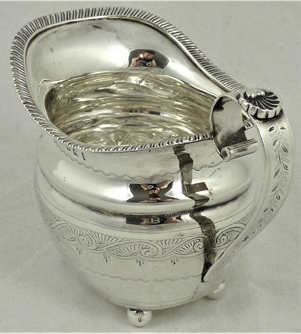 A Victorian sterling silver milk jug featuring gadrooned rim details, engraved geometric scrollwork, a shaped handle, and small ball feet. View III