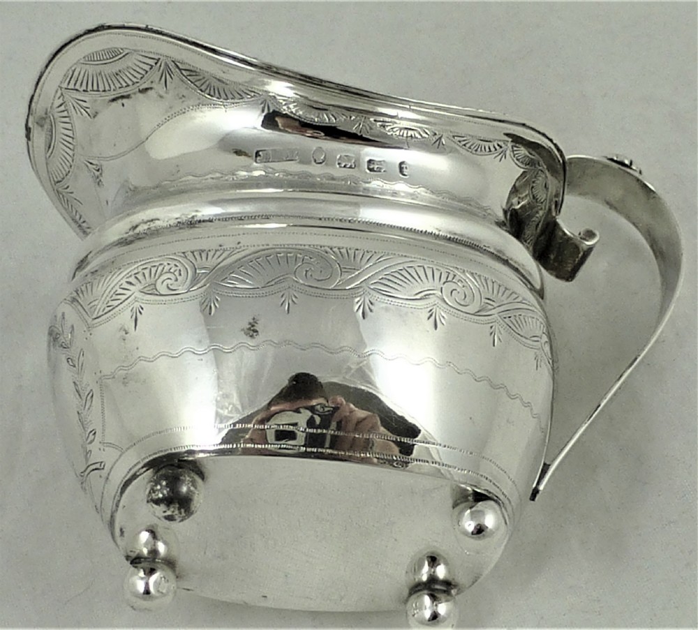 A Victorian sterling silver milk jug featuring gadrooned rim details, engraved geometric scrollwork, a shaped handle, and small ball feet. View VIII
