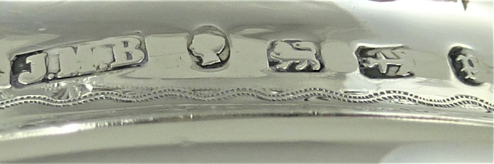 A Victorian sterling silver milk jug featuring gadrooned rim details, engraved geometric scrollwork, a shaped handle, and small ball feet. View IX