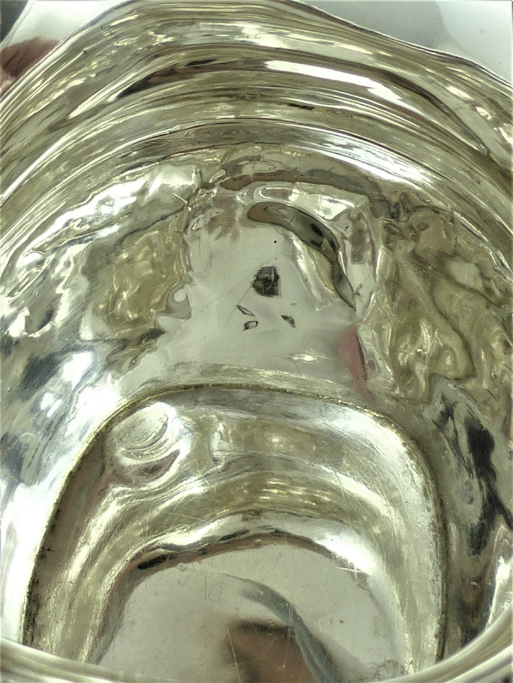 A Victorian sterling silver milk jug featuring gadrooned rim details, engraved geometric scrollwork, a shaped handle, and small ball feet. View XII