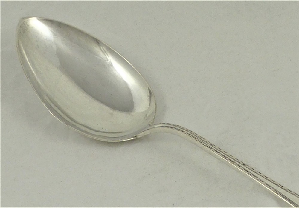 An antique Danish silver serving spoon featuring a polished oval bowl and a tapered stem decorated with bright-cut foliage engraving. View III