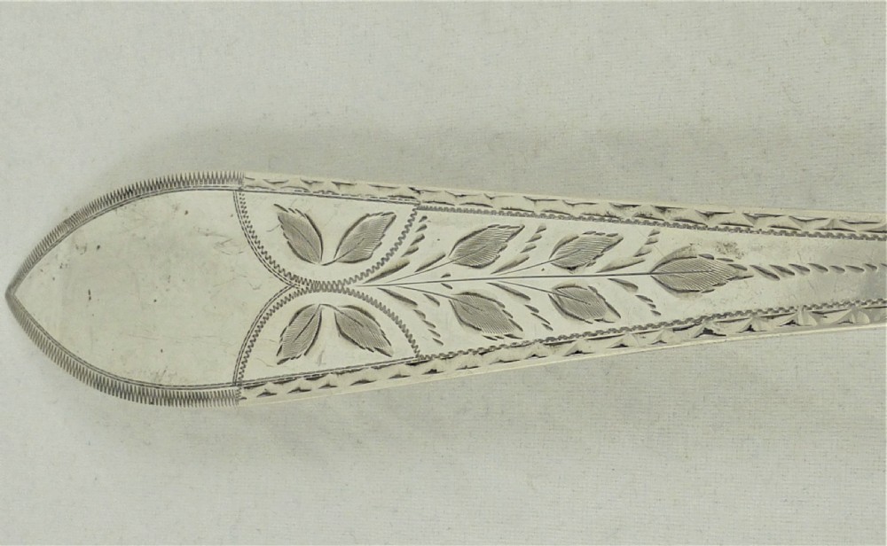 An antique Danish silver serving spoon featuring a polished oval bowl and a tapered stem decorated with bright-cut foliage engraving. View V