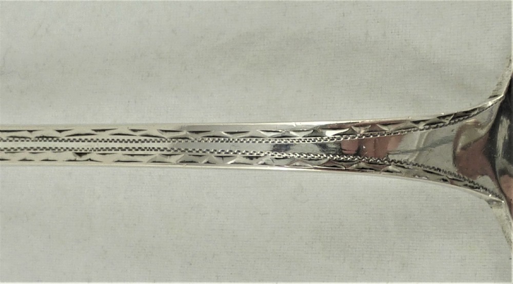 An antique Danish silver serving spoon featuring a polished oval bowl and a tapered stem decorated with bright-cut foliage engraving. View IX