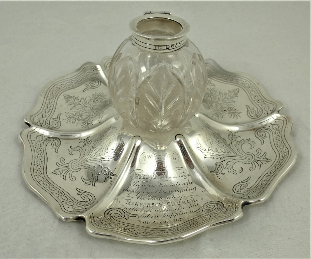 An engraved Victorian sterling silver inkstand featuring a scalloped rim tray and a central cut-glass inkwell with a silver hinged lid.