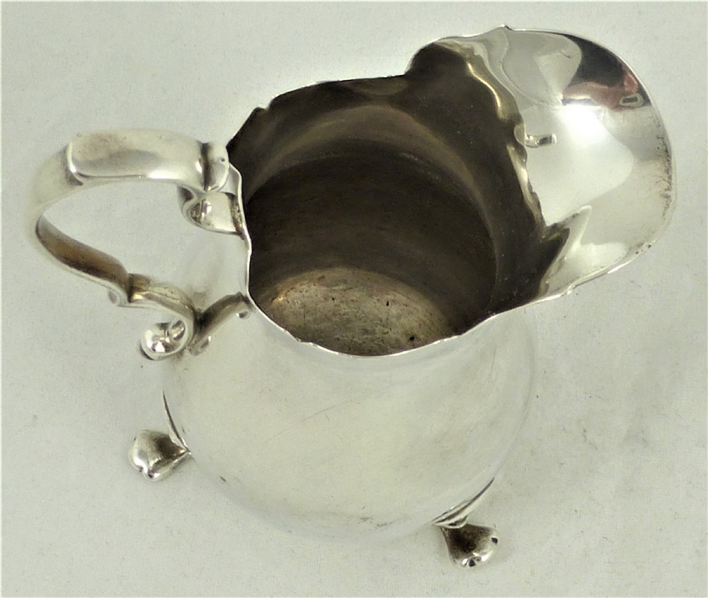 An American sterling silver milk jug featuring a baluster-shaped body, three cabriole legs with pad feet, a double-scroll handle, and a wavy scalloped rim. View VIII