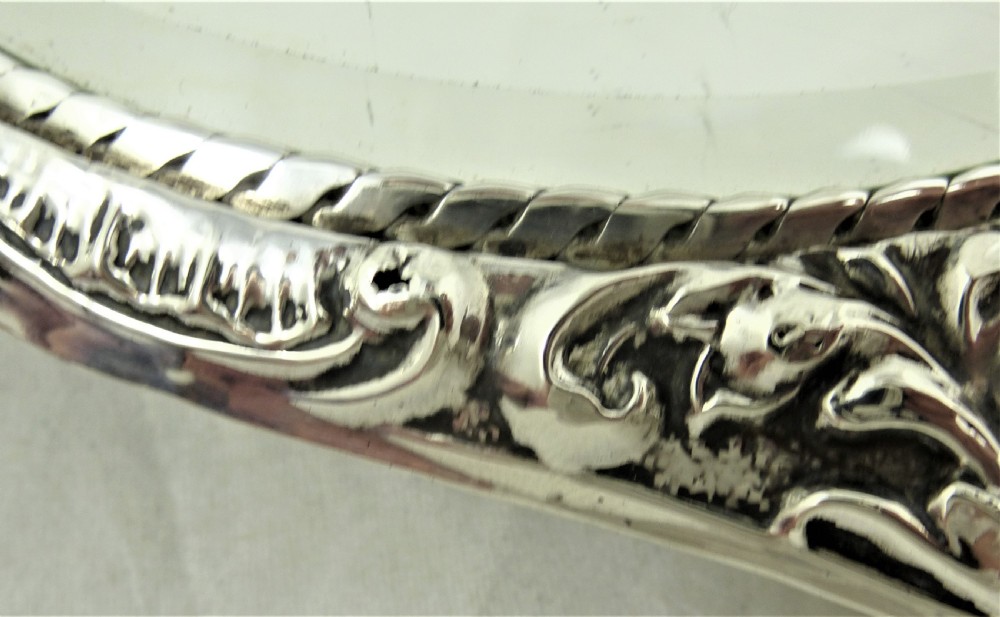 An ornate Edwardian sterling silver hand mirror featuring intricate scrolling foliage repousse decoration and a central engraved monogram. View II