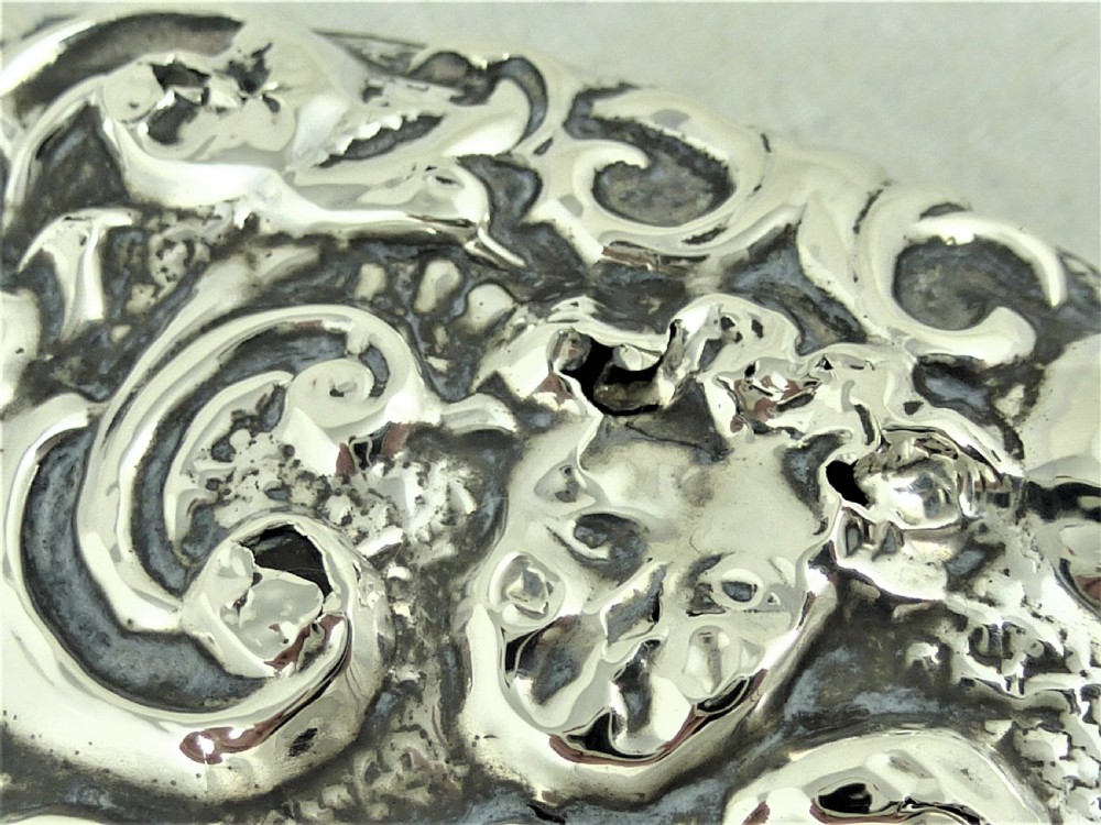 An ornate Edwardian sterling silver hand mirror featuring intricate scrolling foliage repousse decoration and a central engraved monogram. View III