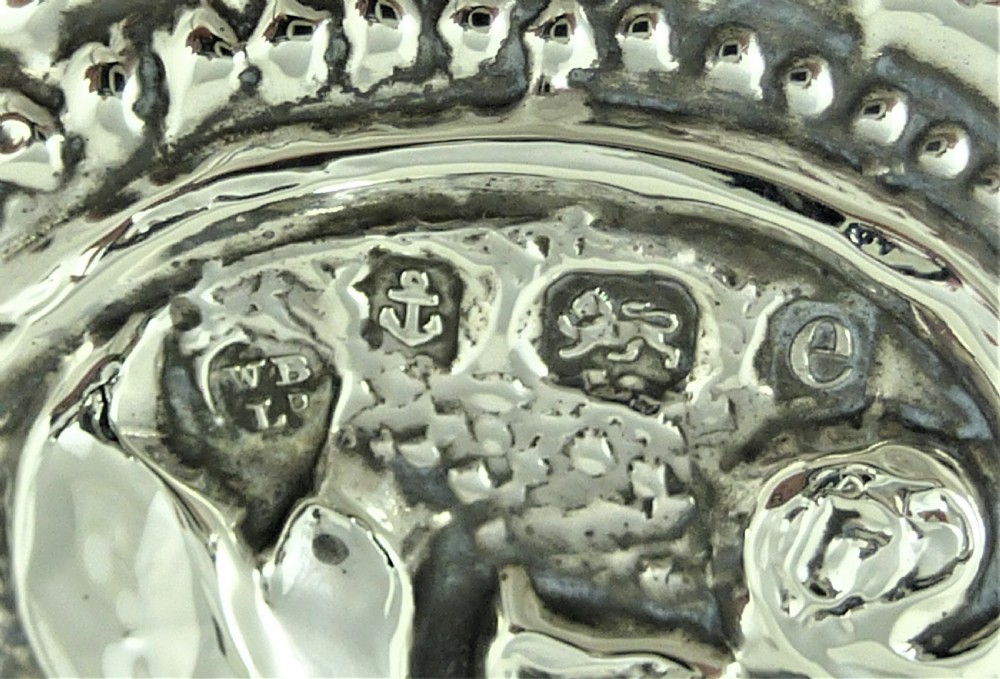 An ornate Edwardian sterling silver hand mirror featuring intricate scrolling foliage repousse decoration and a central engraved monogram. View VII