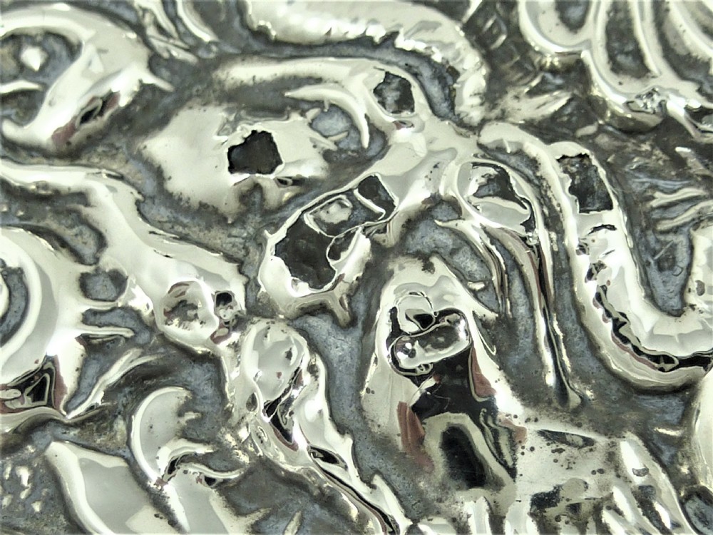 An ornate Edwardian sterling silver hand mirror featuring intricate scrolling foliage repousse decoration and a central engraved monogram. View VIII