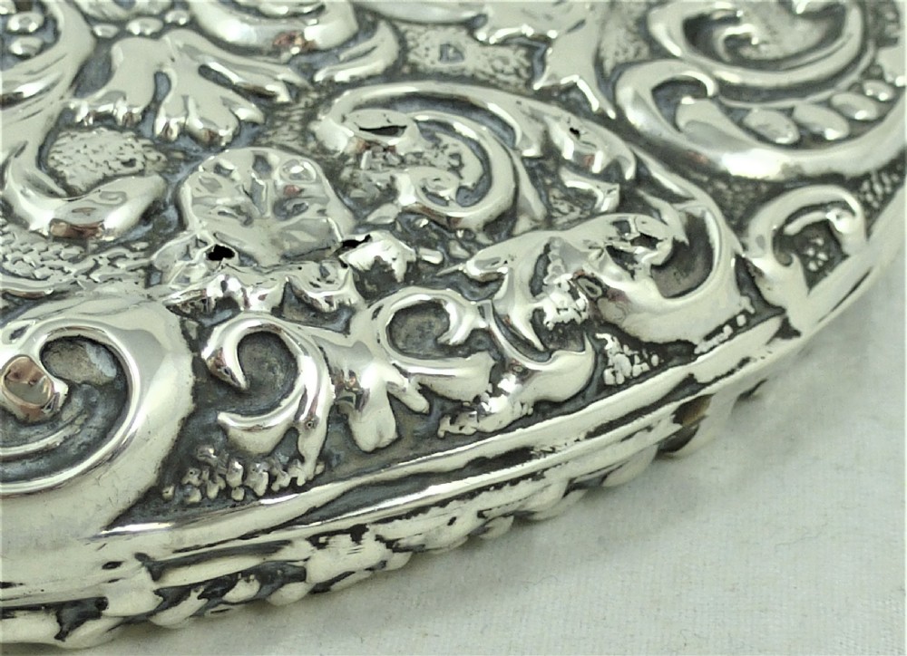 An ornate Edwardian sterling silver hand mirror featuring intricate scrolling foliage repousse decoration and a central engraved monogram. View IX