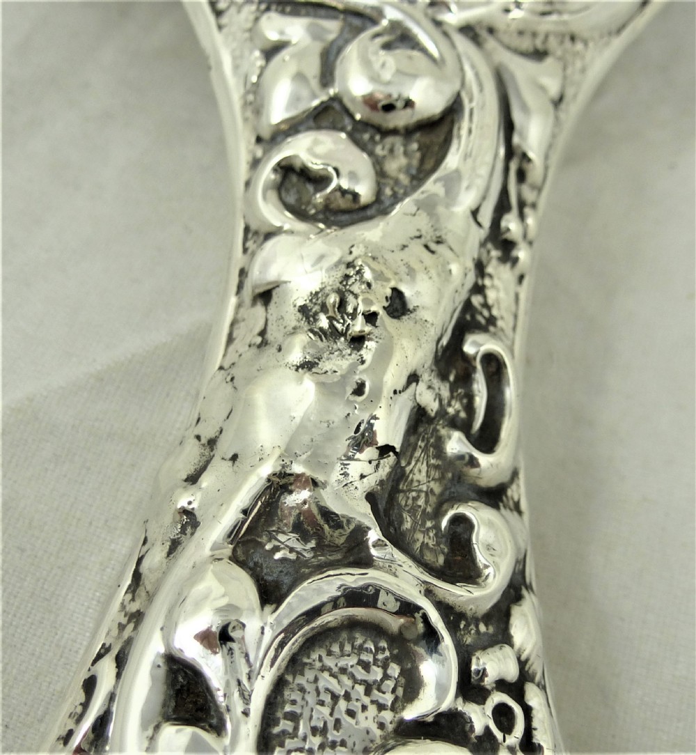 An ornate Edwardian sterling silver hand mirror featuring intricate scrolling foliage repousse decoration and a central engraved monogram. View XIII