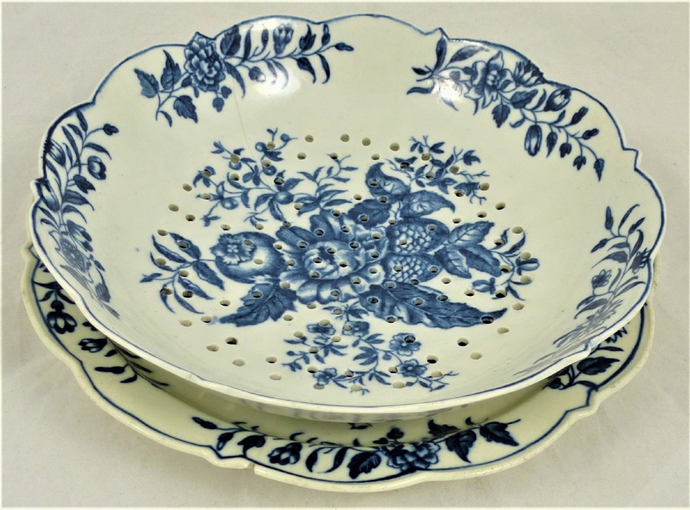 An eighteenth-century blue and white Worcester porcelain strawberry dish with pierced drainage holes resting on a matching scalloped stand.
