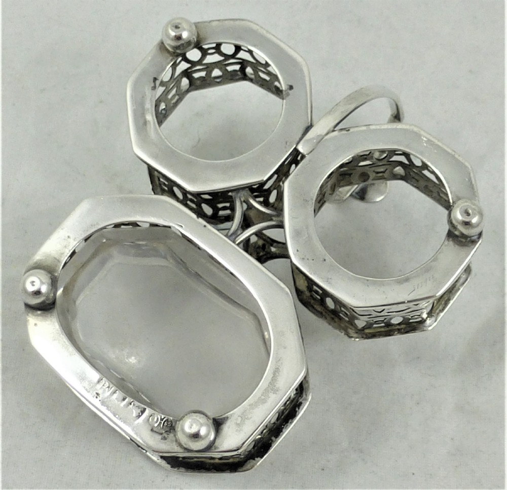A Victorian silver cruet stand featuring three pierced octagonal compartments, small ball feet, an angled central loop handle, and one clear glass insert. View VI