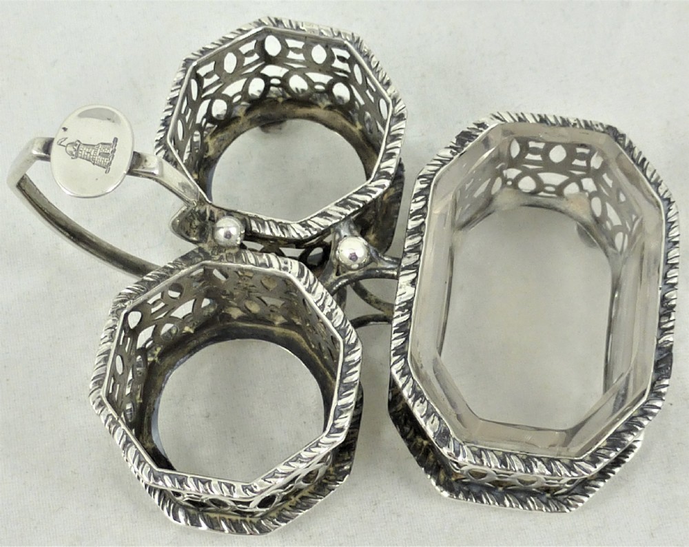 A Victorian silver cruet stand featuring three pierced octagonal compartments, small ball feet, an angled central loop handle, and one clear glass insert. View VII