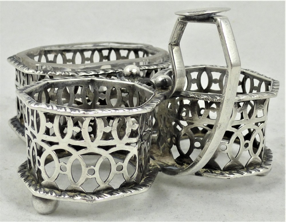 A Victorian silver cruet stand featuring three pierced octagonal compartments, small ball feet, an angled central loop handle, and one clear glass insert. View IX