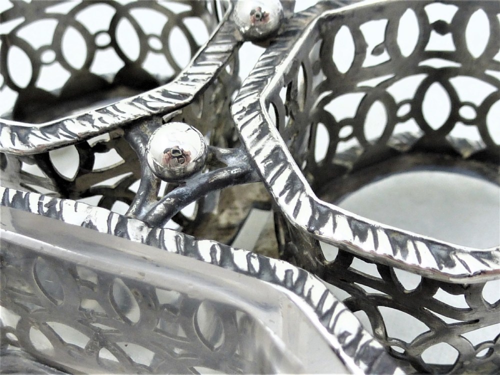 A Victorian silver cruet stand featuring three pierced octagonal compartments, small ball feet, an angled central loop handle, and one clear glass insert. View X