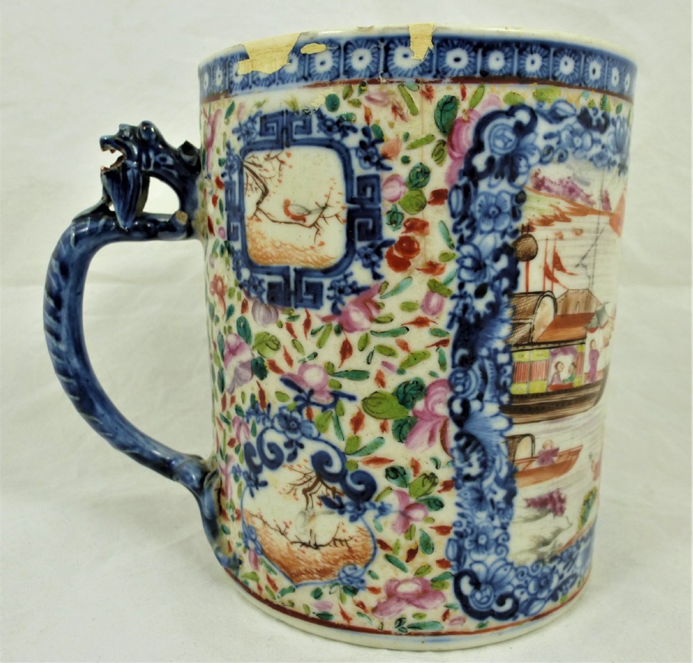 A cylindrical Chinese export porcelain mug featuring a blue dragon-shaped handle, floral enamels, and cartouches depicting figures on boats.