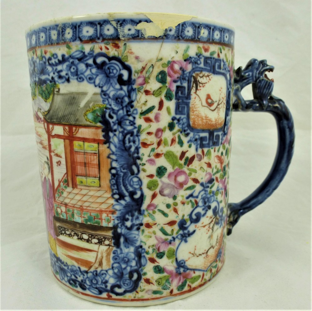A cylindrical Chinese export porcelain mug featuring a blue dragon-shaped handle, floral enamels, and cartouches depicting figures on boats. View II