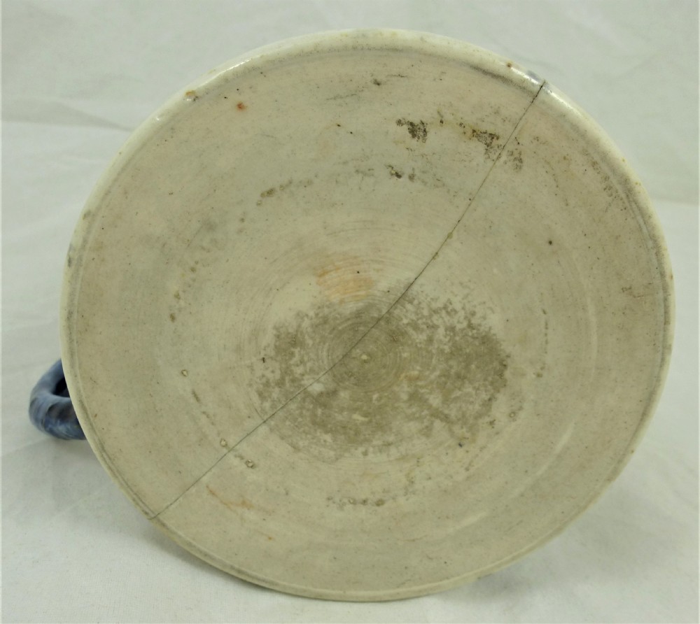 A cylindrical Chinese export porcelain mug featuring a blue dragon-shaped handle, floral enamels, and cartouches depicting figures on boats. View V
