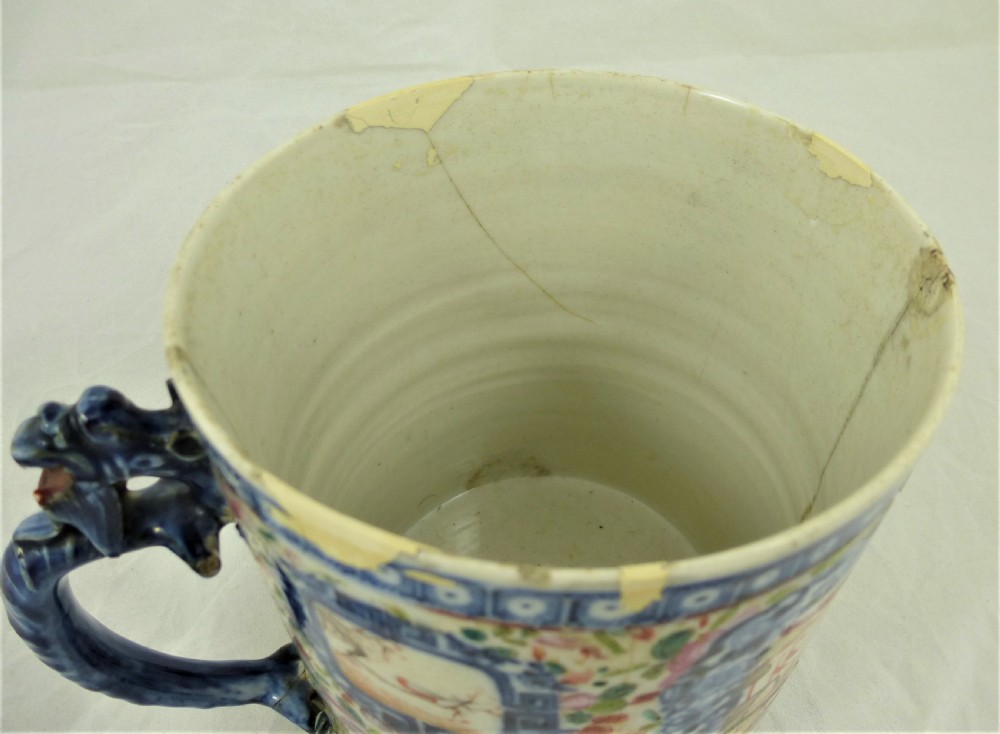 A cylindrical Chinese export porcelain mug featuring a blue dragon-shaped handle, floral enamels, and cartouches depicting figures on boats. View VI