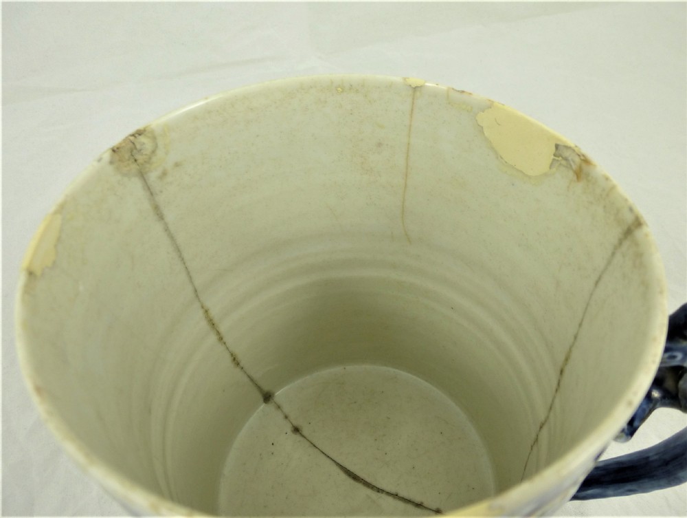 A cylindrical Chinese export porcelain mug featuring a blue dragon-shaped handle, floral enamels, and cartouches depicting figures on boats. View VII