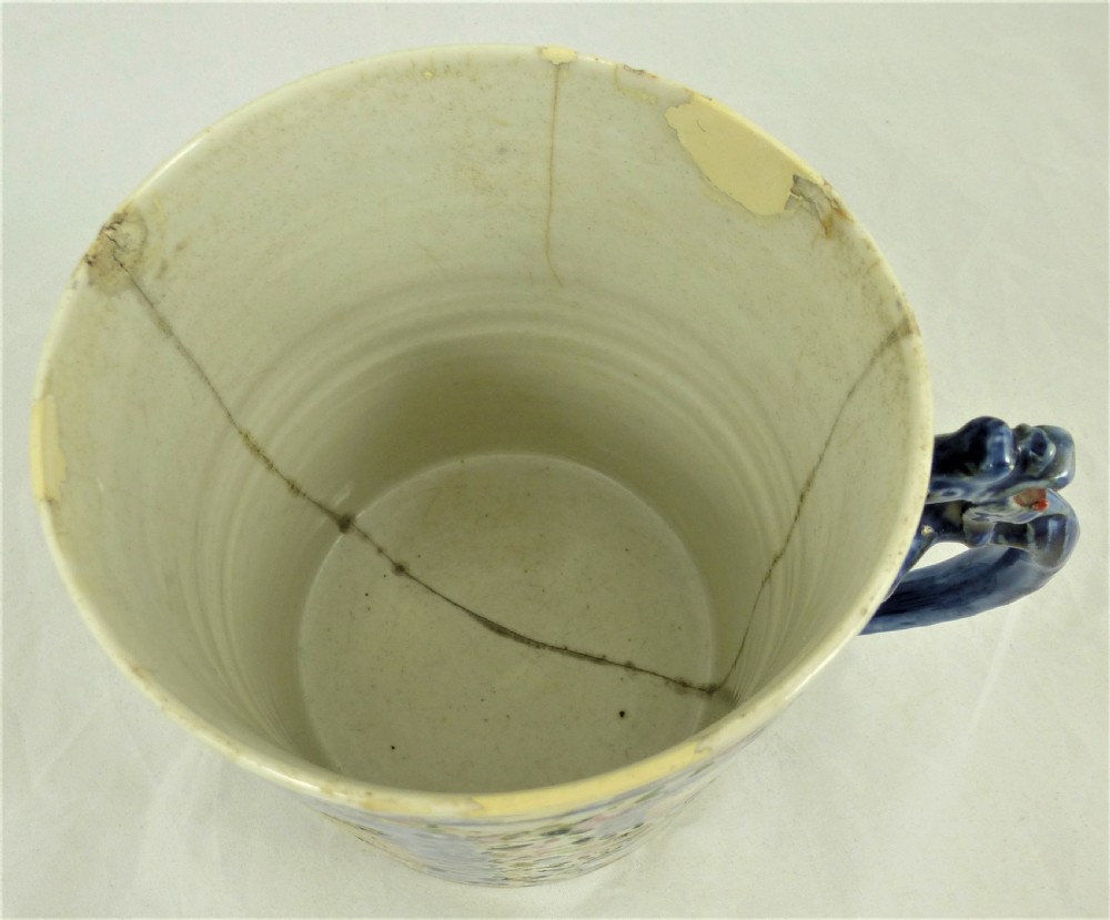 A cylindrical Chinese export porcelain mug featuring a blue dragon-shaped handle, floral enamels, and cartouches depicting figures on boats. View VIII