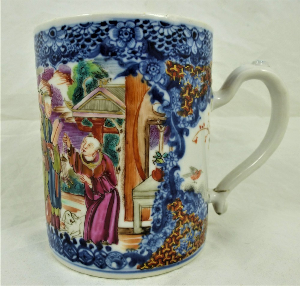 A cylindrical porcelain mug decorated with hand-painted figures in polychrome enamels surrounded by a blue underglaze floral border and fitted with a moulded handle.
