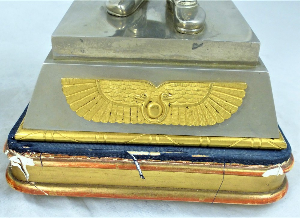 A pair of silvered and gilt metal statuettes depicting an ancient Assyrian king and queen standing on stepped plinths adorned with winged sun motifs. View V