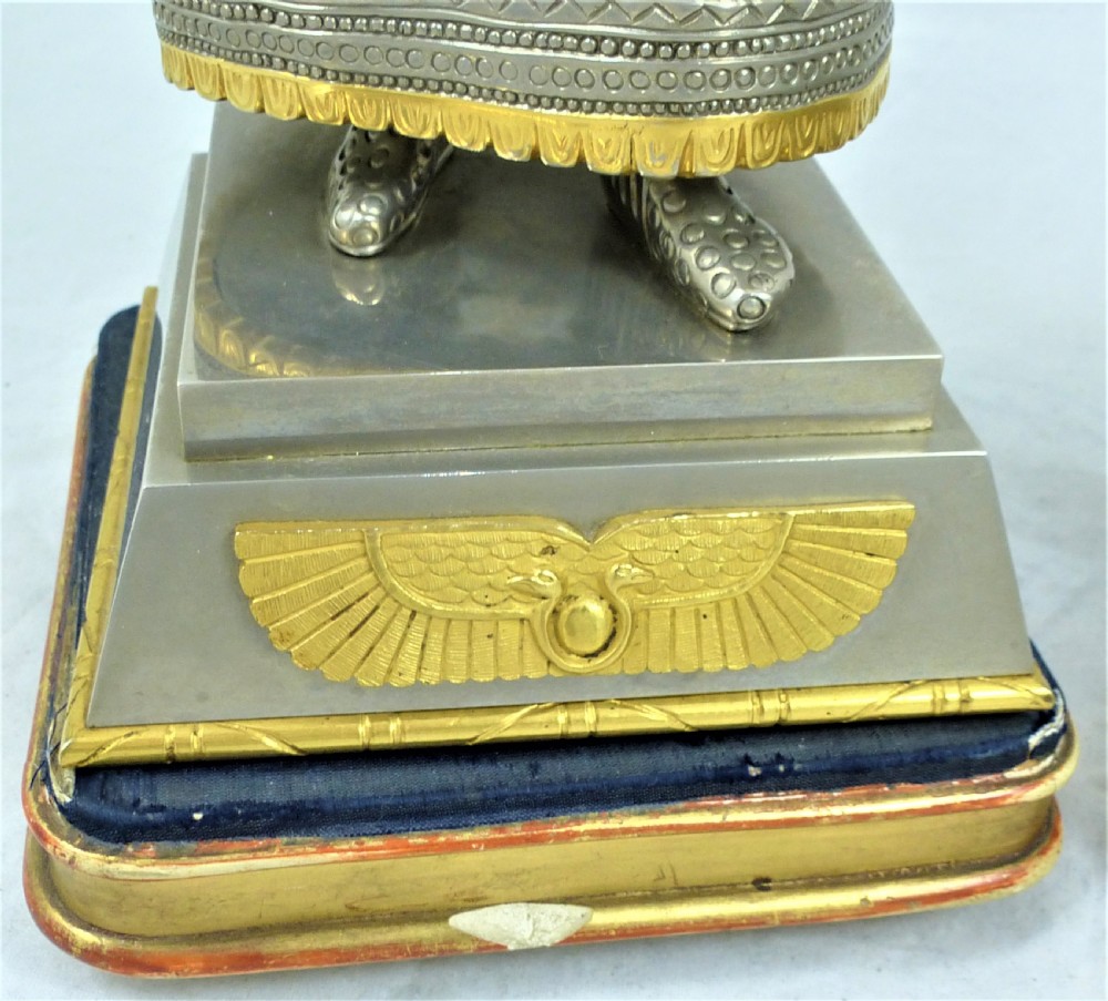 A pair of silvered and gilt metal statuettes depicting an ancient Assyrian king and queen standing on stepped plinths adorned with winged sun motifs. View VI