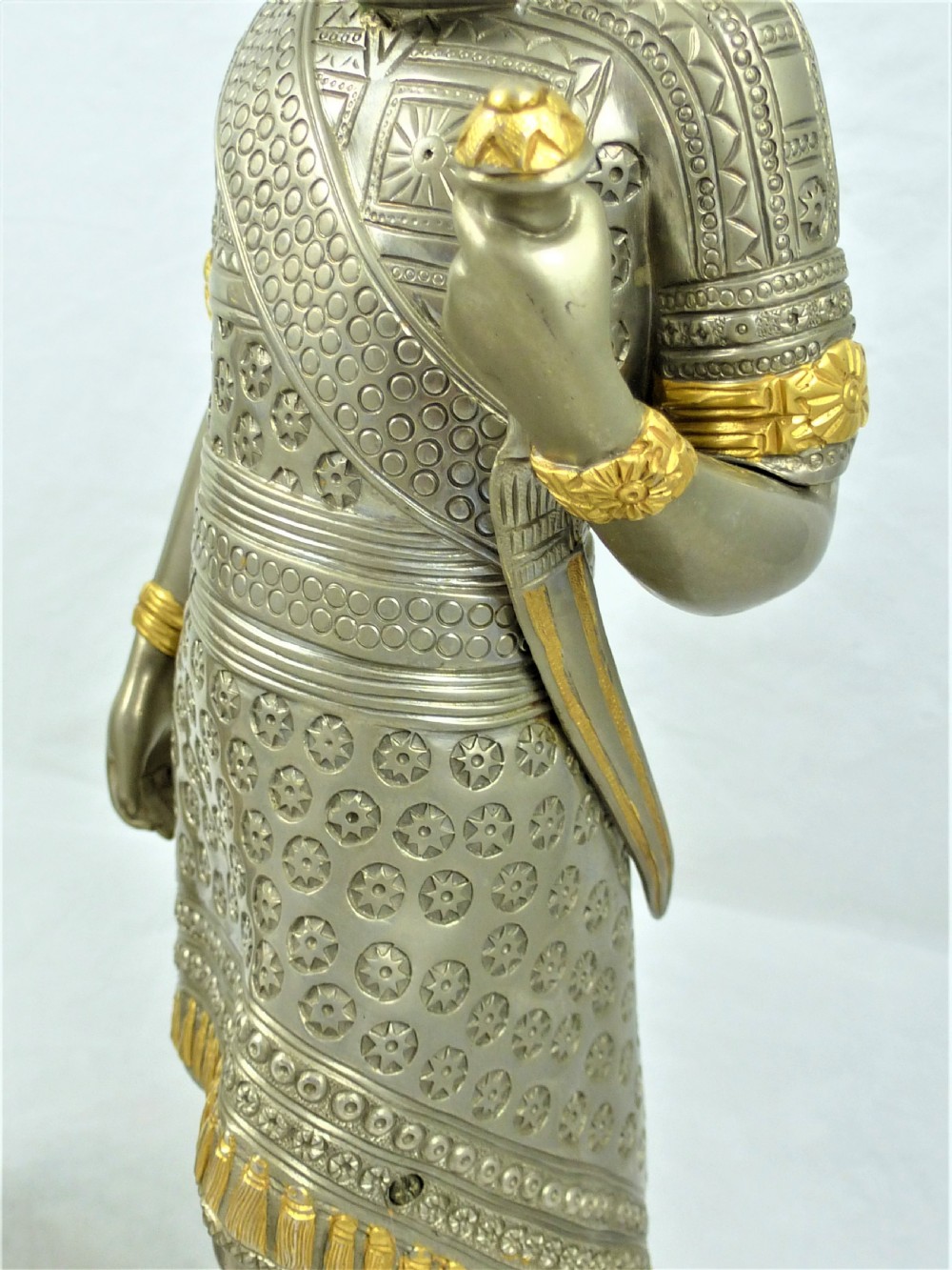 A pair of silvered and gilt metal statuettes depicting an ancient Assyrian king and queen standing on stepped plinths adorned with winged sun motifs. View VIII