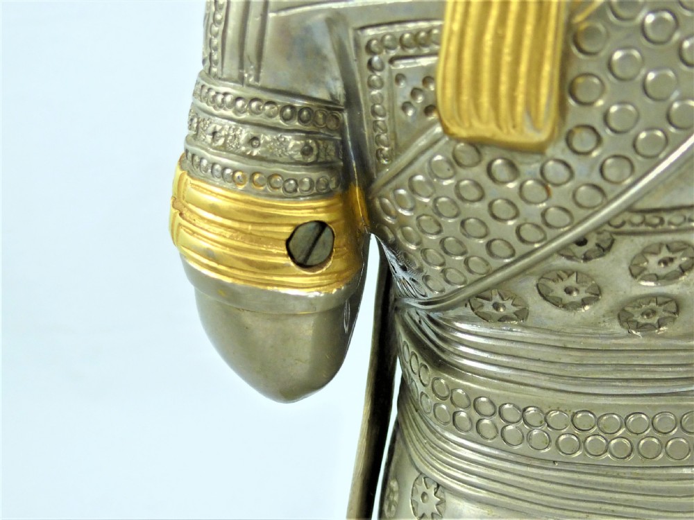 A pair of silvered and gilt metal statuettes depicting an ancient Assyrian king and queen standing on stepped plinths adorned with winged sun motifs. View XIX