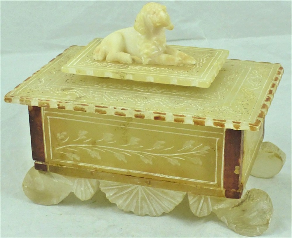 A 19th-century carved cream alabaster trinket box featuring a reclining dog figure on the lid, incised leaf motifs on the front panel, and fan-shaped feet.