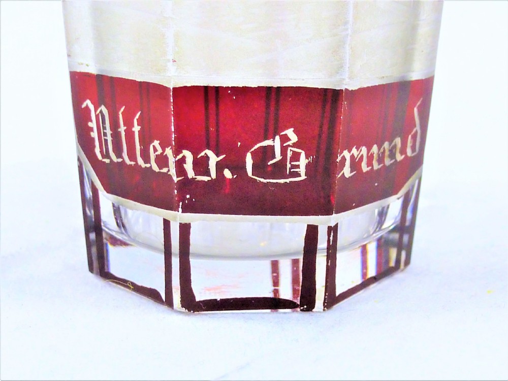 A small faceted glass shot glass featuring a ruby red flashed coating etched with a building scene and German script text. View II