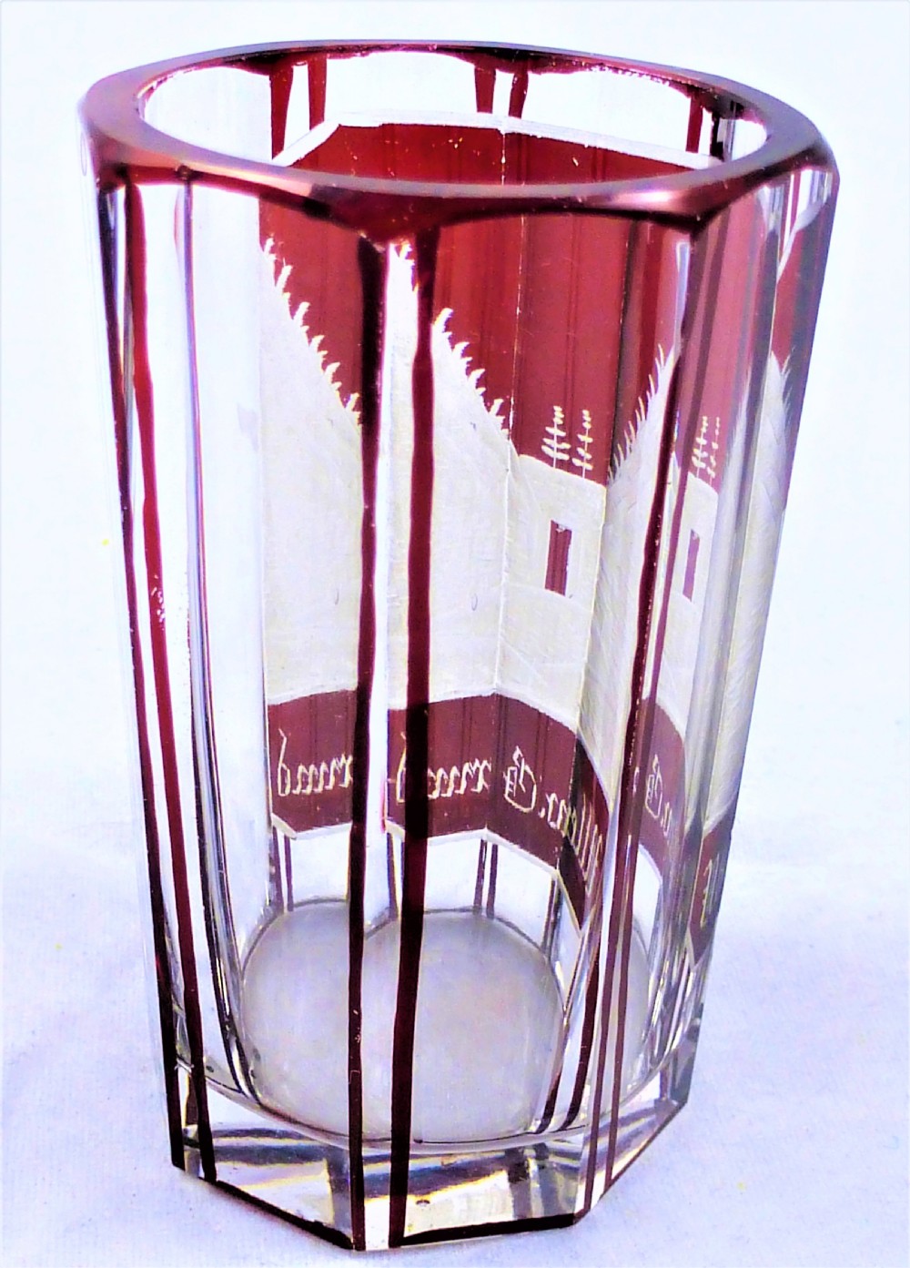 A small faceted glass shot glass featuring a ruby red flashed coating etched with a building scene and German script text. View III