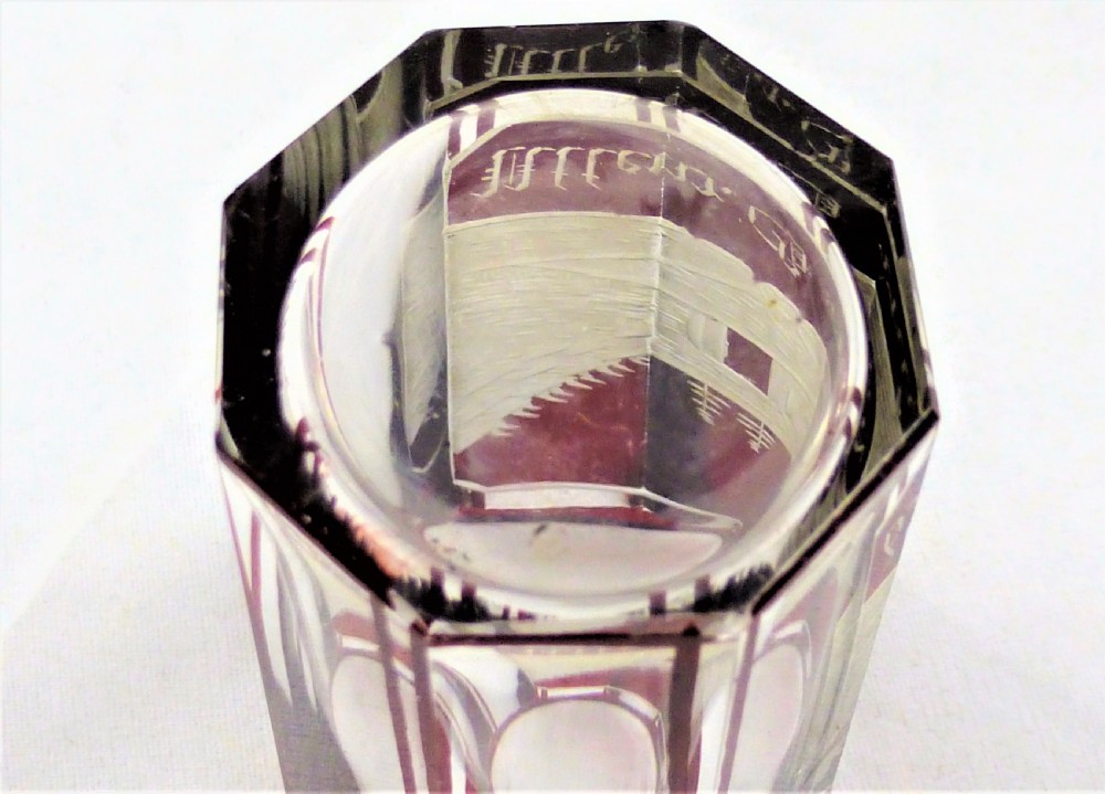 A small faceted glass shot glass featuring a ruby red flashed coating etched with a building scene and German script text. View VI