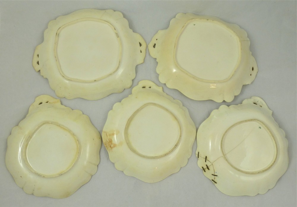 A five-piece English Rococo porcelain dessert service featuring cream-coloured shaped dishes hand-painted with green foliage, floral motifs, and gilt scalloped rims. View II