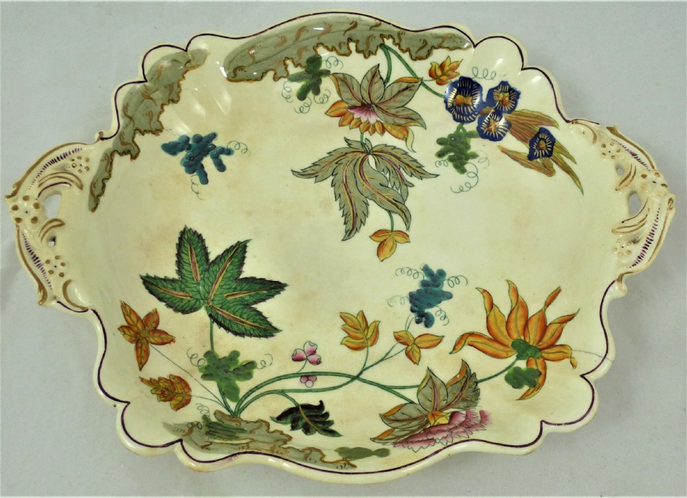 A five-piece English Rococo porcelain dessert service featuring cream-coloured shaped dishes hand-painted with green foliage, floral motifs, and gilt scalloped rims. View X