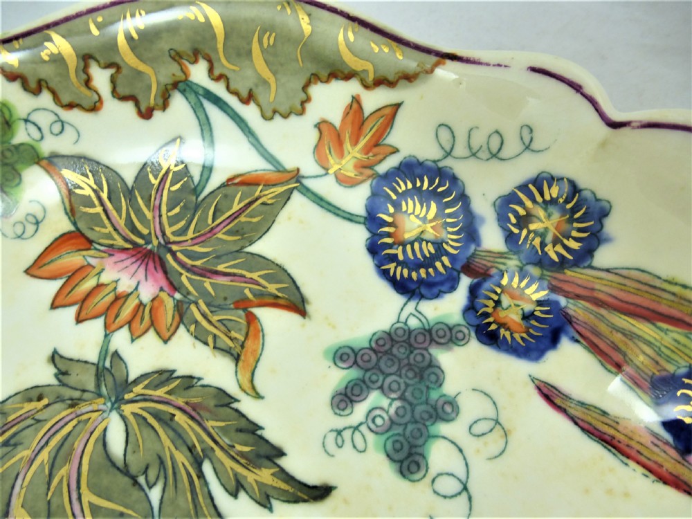 A five-piece English Rococo porcelain dessert service featuring cream-coloured shaped dishes hand-painted with green foliage, floral motifs, and gilt scalloped rims. View XVII