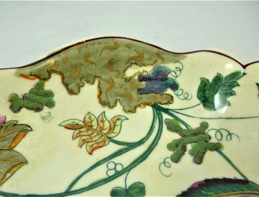 A five-piece English Rococo porcelain dessert service featuring cream-coloured shaped dishes hand-painted with green foliage, floral motifs, and gilt scalloped rims. View XXI
