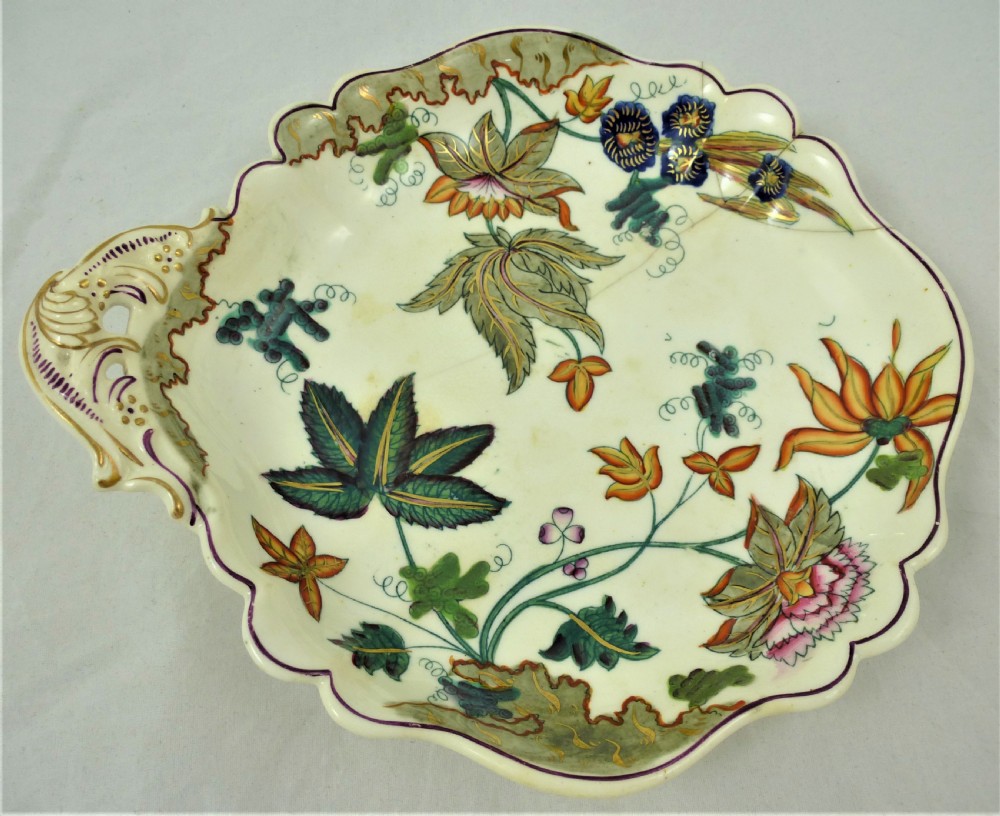 A five-piece English Rococo porcelain dessert service featuring cream-coloured shaped dishes hand-painted with green foliage, floral motifs, and gilt scalloped rims. View XXV