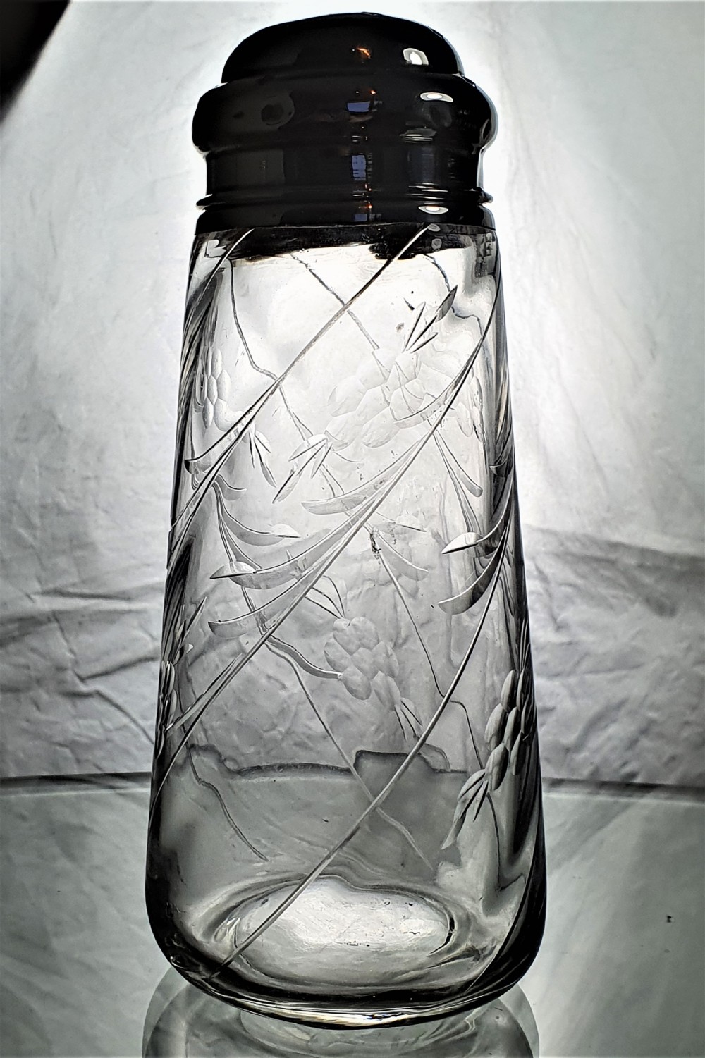 A tapered clear cut-glass sugar shaker featuring etched floral motifs and a domed, perforated silver cap.